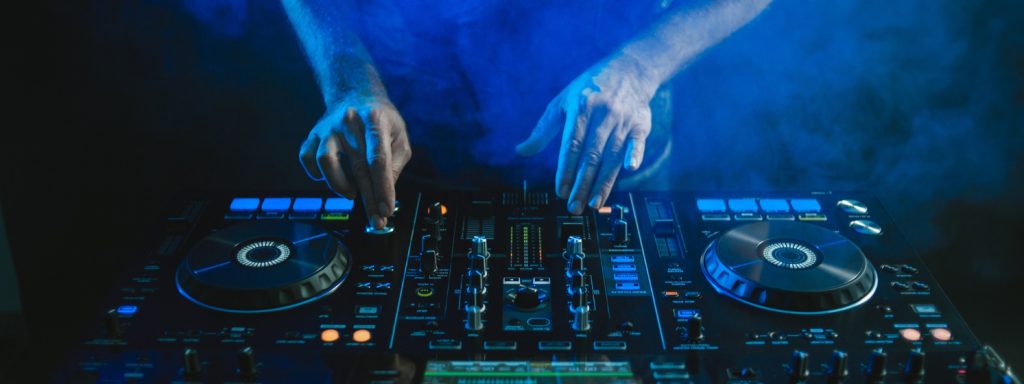 DJ tocando música electrónica en una consola profesional en un evento de Kovak Collective, rodeado de efectos de humo y luces